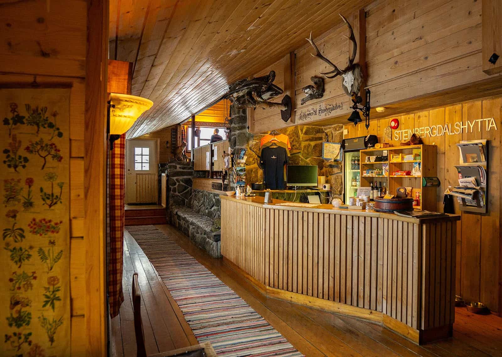 Interior reception area of Steinbergdalshytta lodge with wood paneling, stone accents, and mounted antlers.