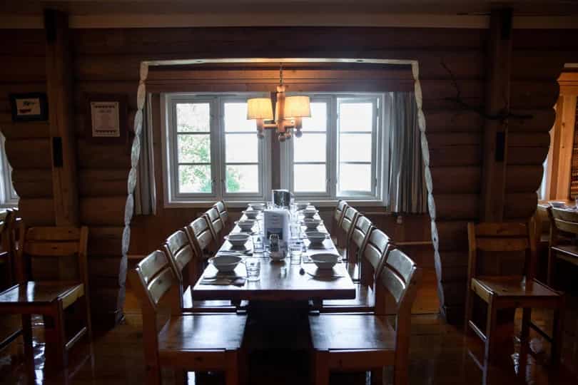 Dining hall with long wooden table set for a meal inside a log cabin structure, Bjørnhollia.