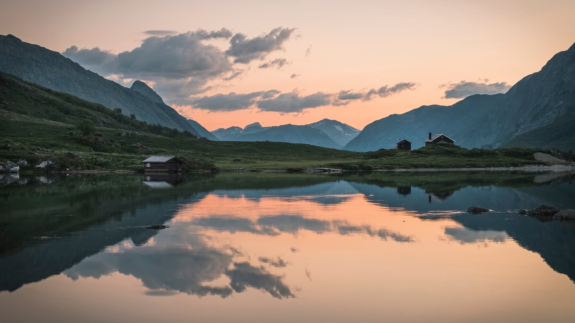 Mountain lake reflecting cabins and sunset sky with clouds near Gjende Lake.