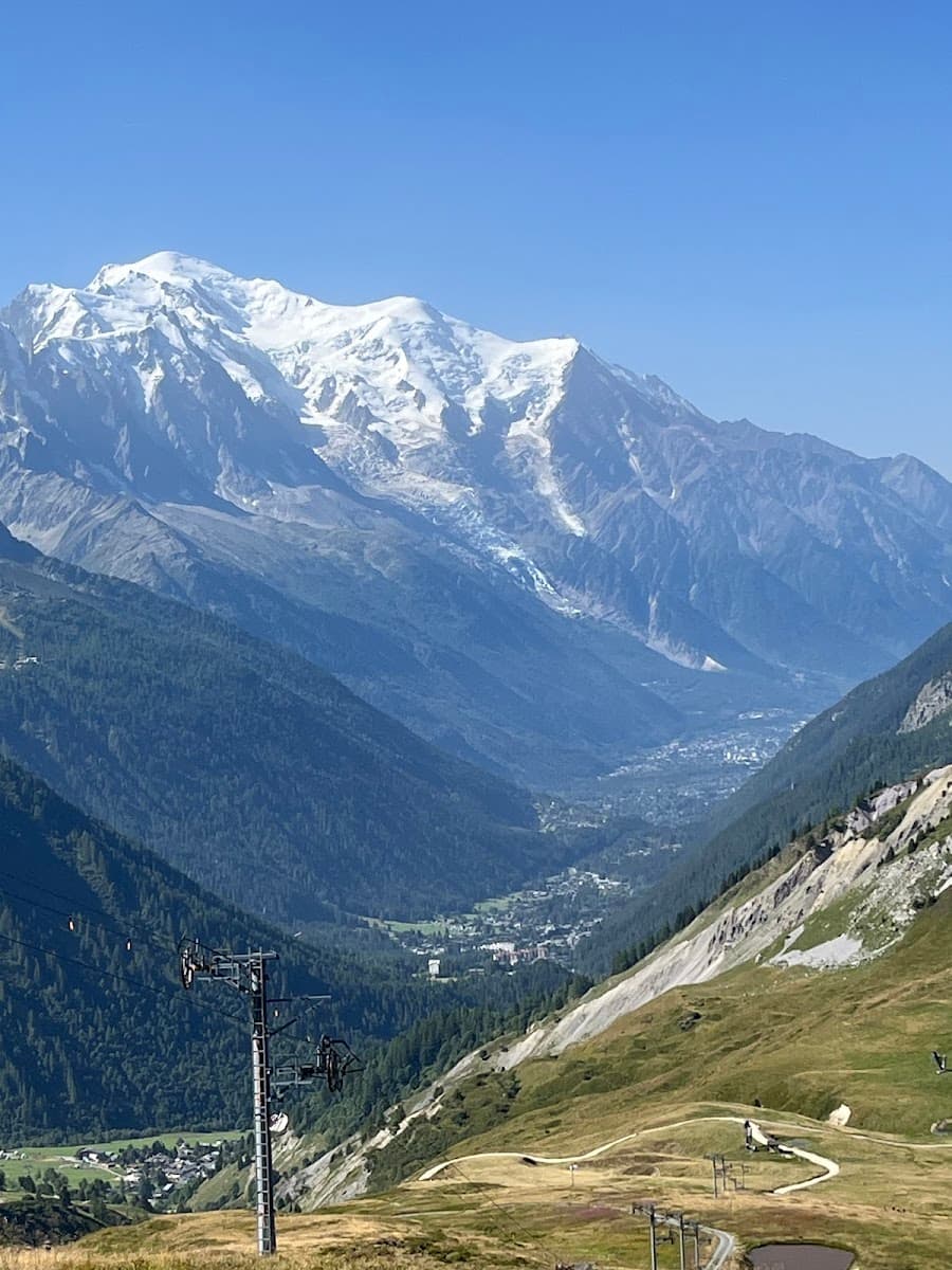 Snow-capped mountains towering over a deep valley with a village and ski lift tower in the foreground.