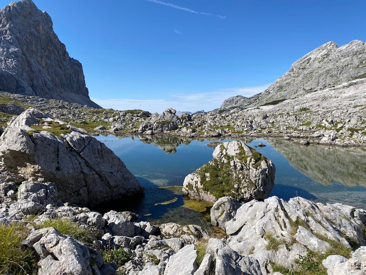 Alpine tarn reflecting steep, rocky mountains under a clear blue sky