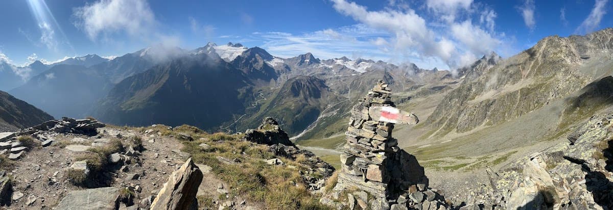 Hiking cairn with trail marker overlooking high alpine mountains and valley road.