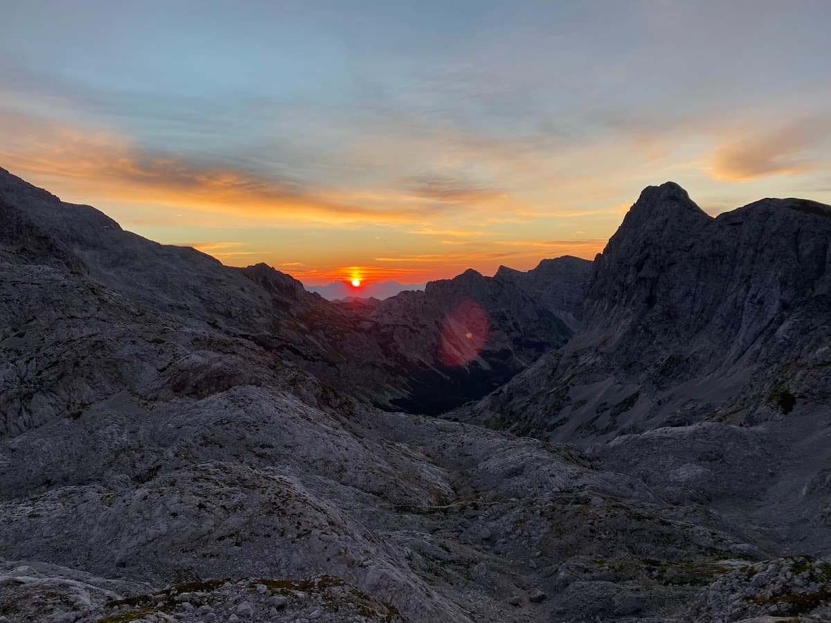 Rocky mountain peaks at sunrise with orange and blue sky over a deep valley.