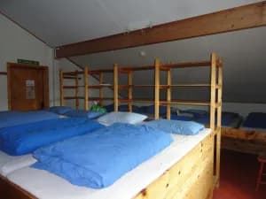 Dormitory room with wooden bunk beds, white mattresses, and blue duvets at Rondvassbu.