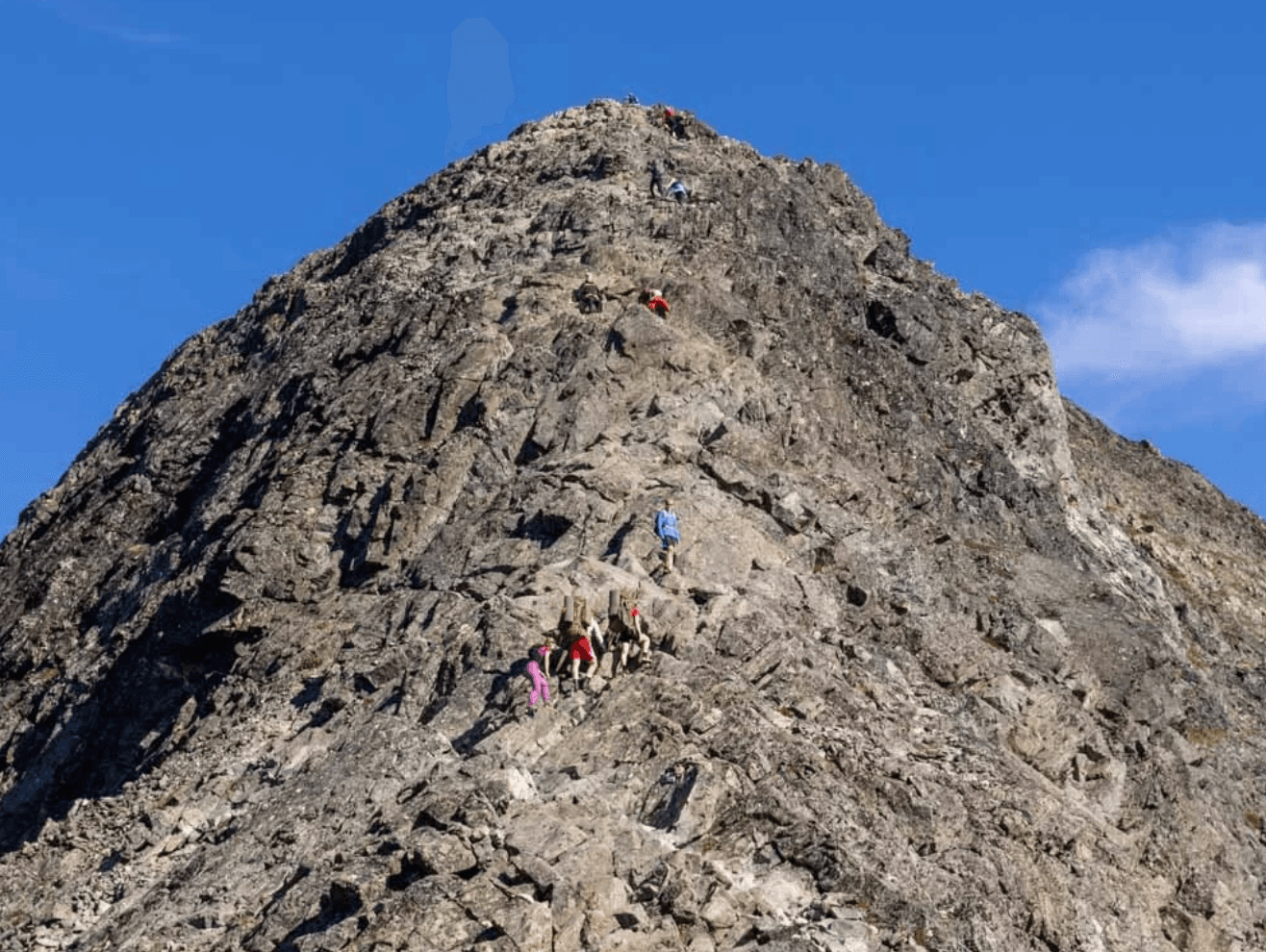 Hikers climbing a steep, rocky mountain peak in Jotunheimen, Norway.