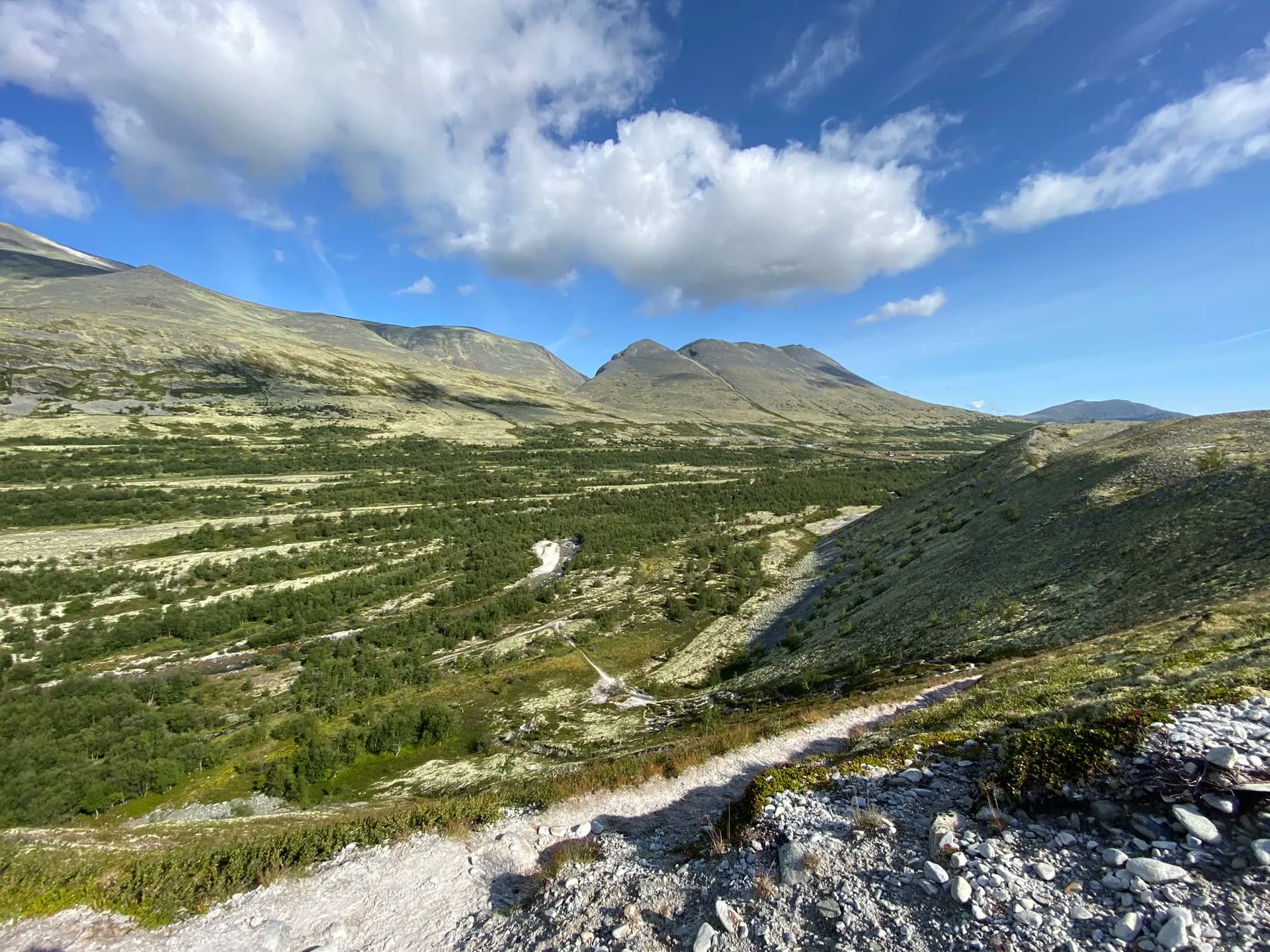 Mountain landscape in Rondane National Park with a hiking trail, green valley, and rocky slopes under a blue sky.