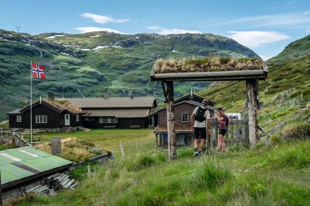 Wanderer, die bei Steinbergdalshytta ankommen, einer mit Gras bedeckten Lodge im Aurlandsdalen, die die norwegische Flagge hisst