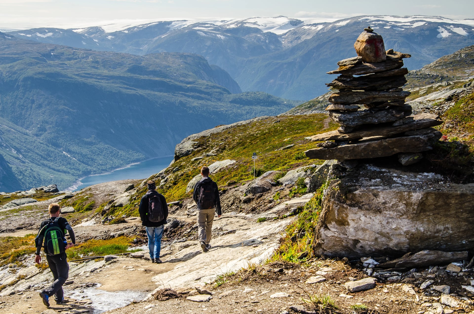 Drei Männer wandern auf dem Trolltunga-Weg mit einer Felsformation im Vordergrund