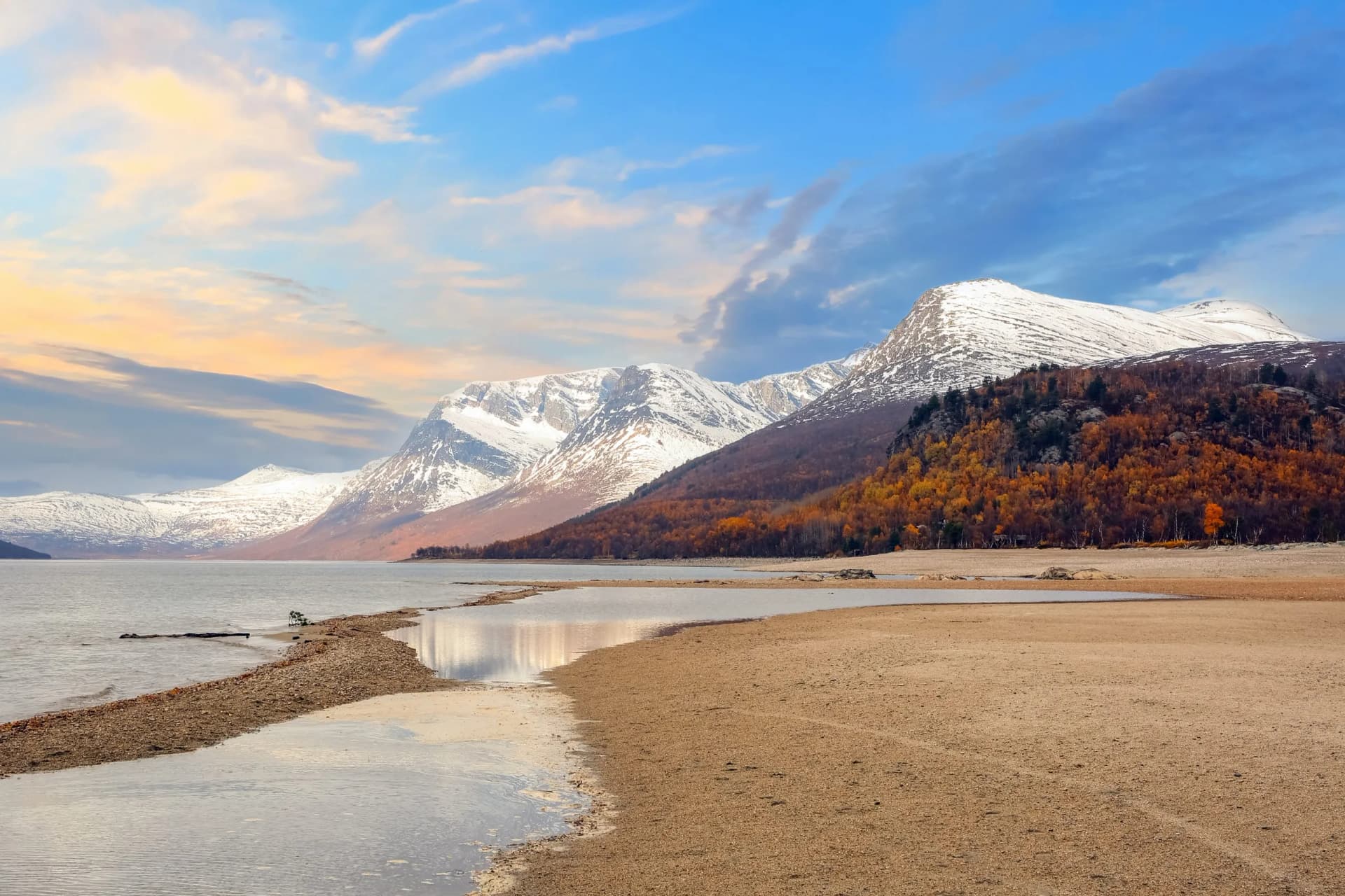 Lake Gjevillvatnet with snow-capped mountains and autumn foliage under a blue sky.