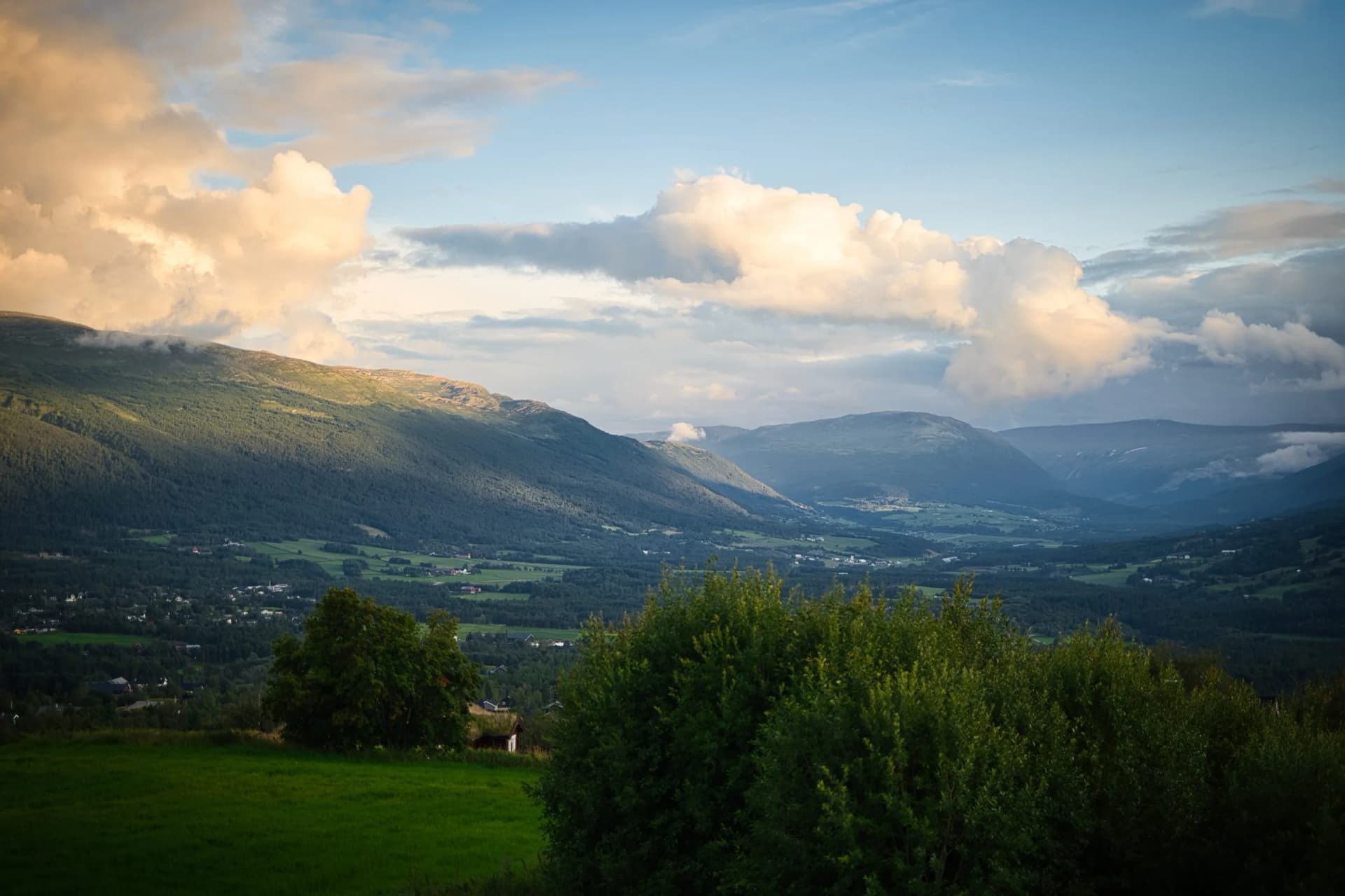 Rural hills of Oppdal valley under bright, cloudy sky with green foreground.