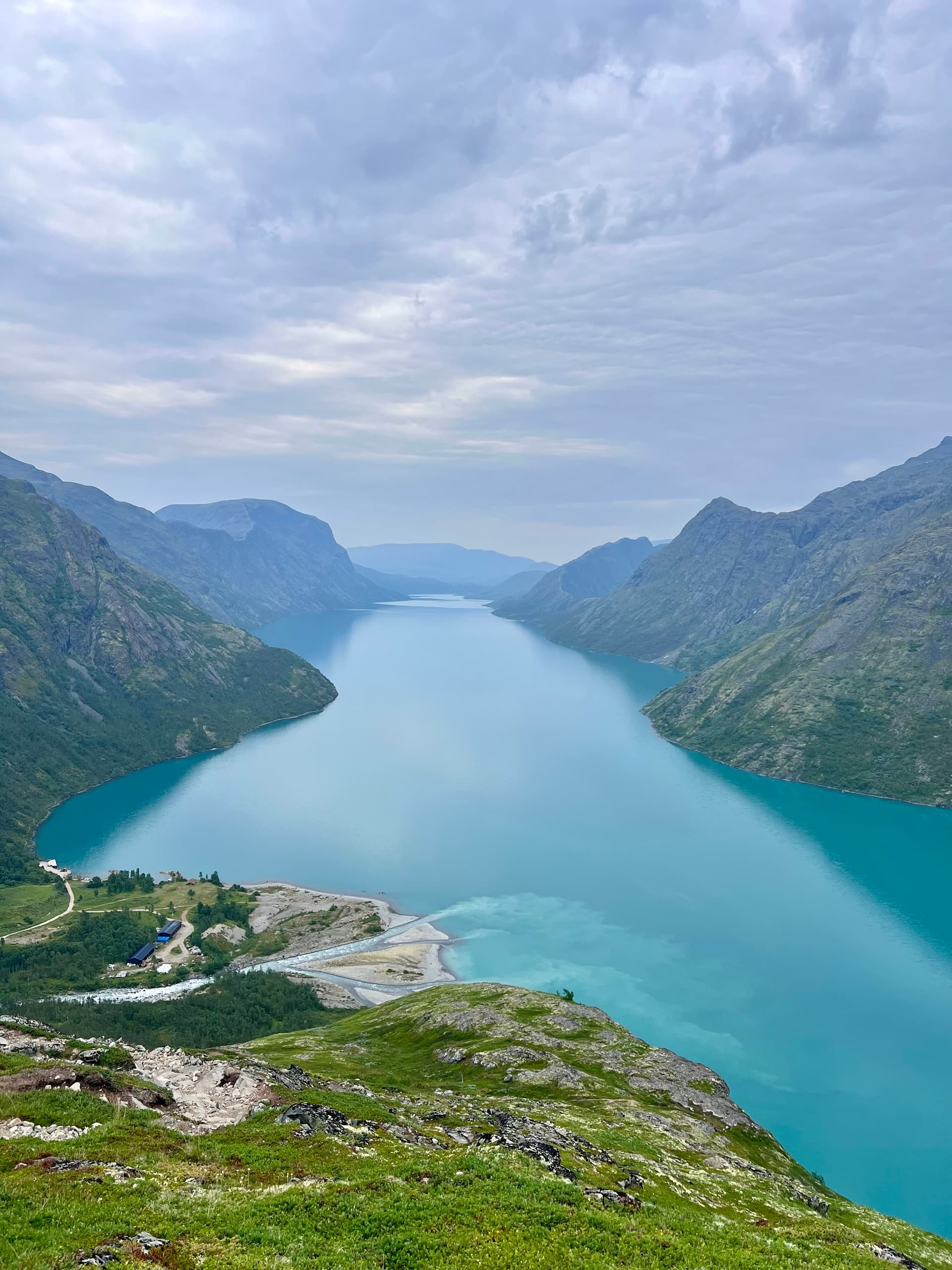 Turquoise alpine lake viewed from above between steep mountain slopes under a cloudy sky