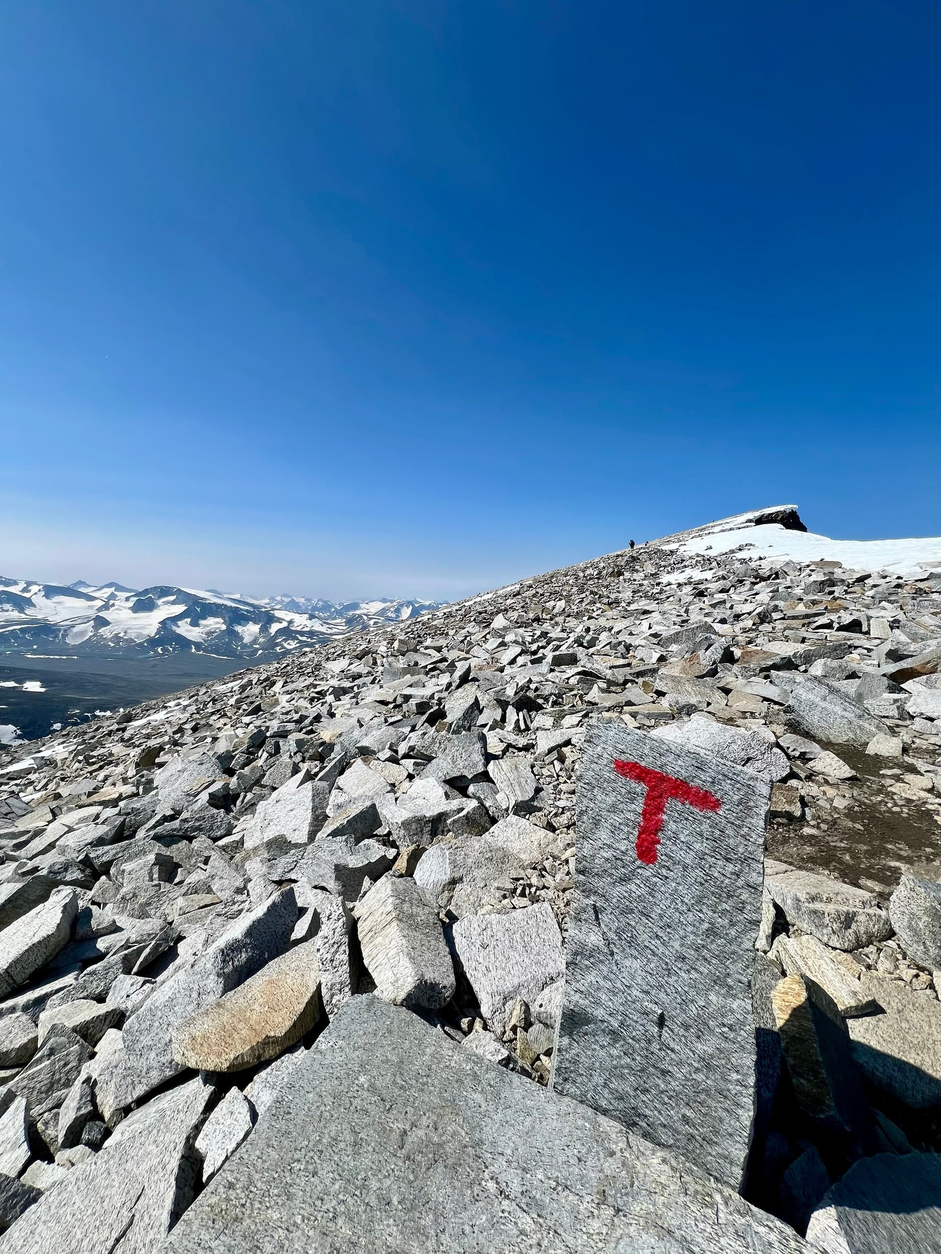 Red trail marker on rock in rocky mountain landscape under blue sky