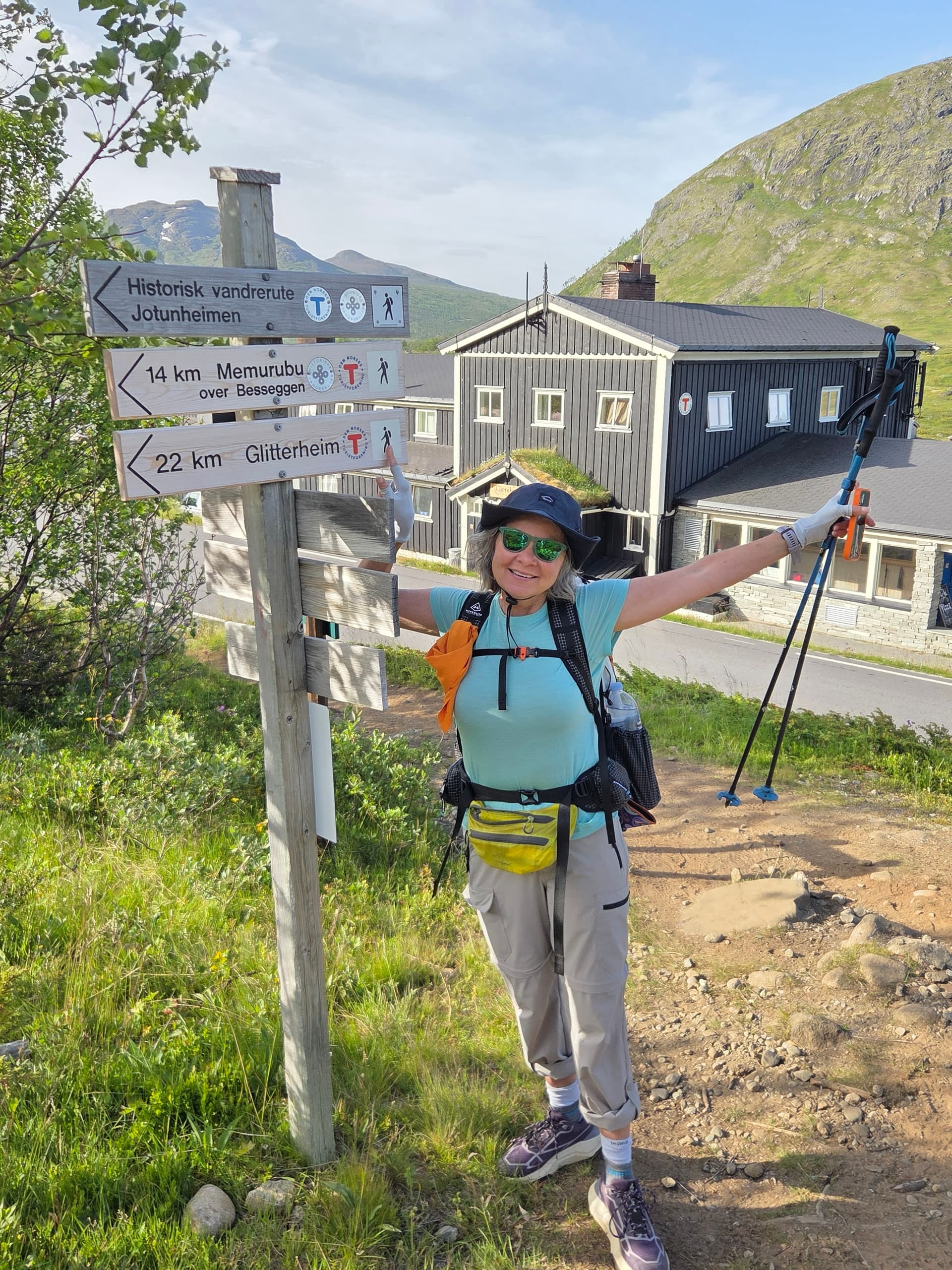 Hiker standing next to a wooden trail signpost with mountain lodge in background