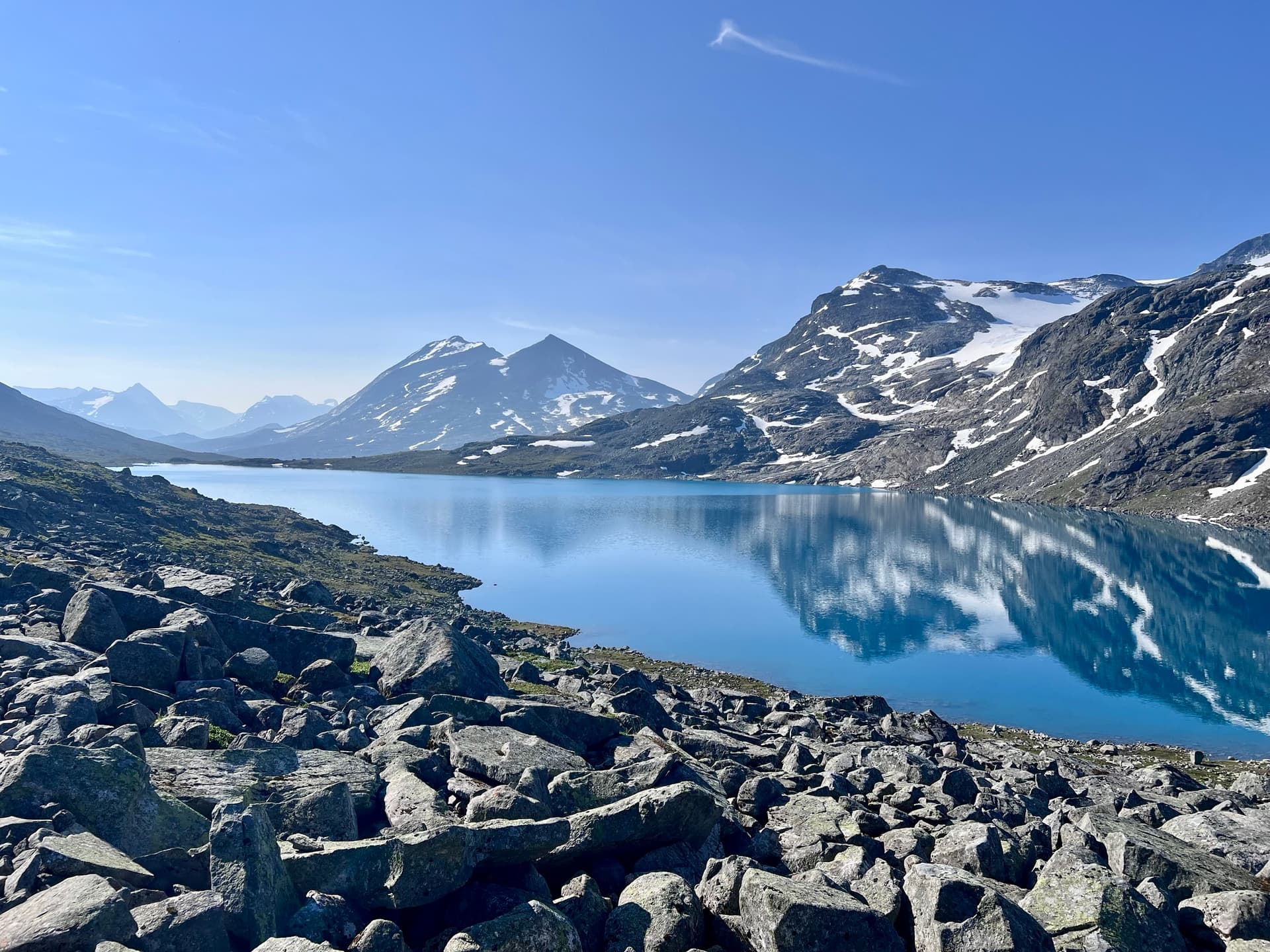 Alpine mountain lake with snow-capped peaks and rocky shoreline reflecting in blue water