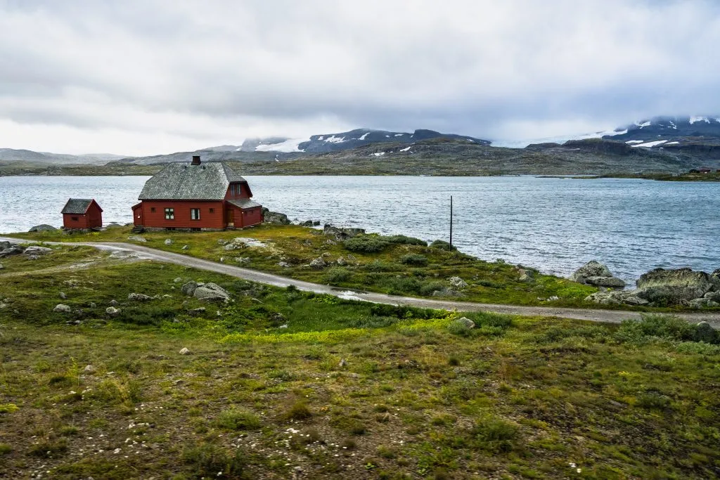 Ein einsames Haus an einem See im Hardangervidda-Nationalpark bei Finse, Norwegen. Das Foto wurde aus dem Zug Oslo-Bergen aufgenommen, einer der spektakulärsten Eisenbahnstrecken Europas.